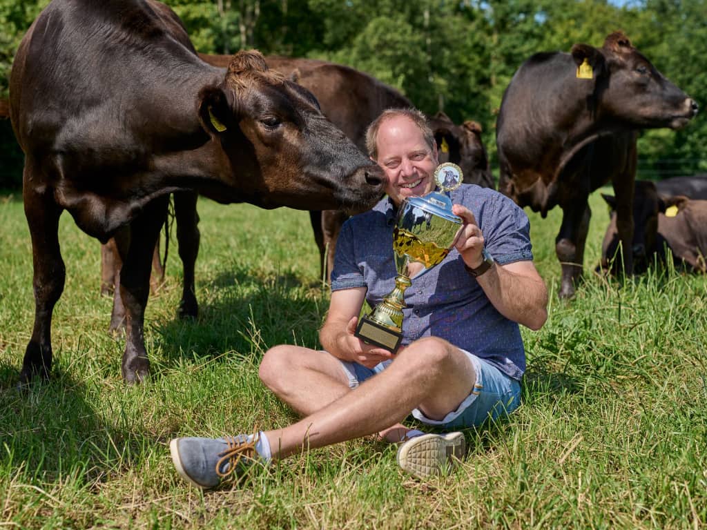 Patrick Balster hält einen Pokal für seine preisgekrönte Wagyu-Zucht inmitten seiner Rinder auf der Weide.